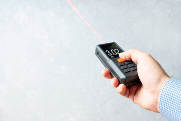 Laser rangefinder or laser tape measure in a male hand. It is a smart device for quick measurement of a distance. Background with copy space. - obrazy, fototapety, plakaty