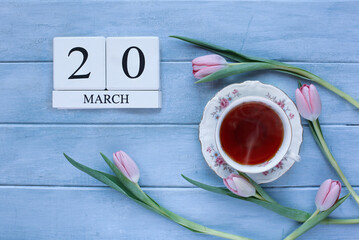 White wood calendar blocks with the date March 20th with tea and pink tulips for the first day of spring.  Spring equinox.