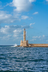 Lighthouse in the old venecian port in Chania, Crete during sunny summer day with blue splashing sea and blue sky