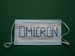 Face mask with word Omicron written on it and green background with copy space