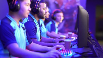 Group of multiethnic cybersport players in headsets sitting in front of computers and playing video games online indoors