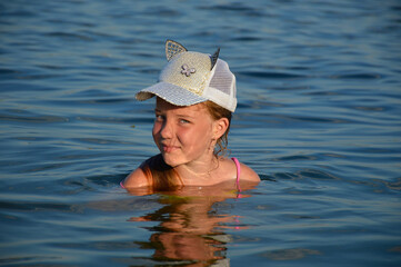 Natural portrait of a young Caucasian woman, without skin retouching, without color correction. Portrait of a girl outdoors in the water, blonde in a baseball cap, naturalness