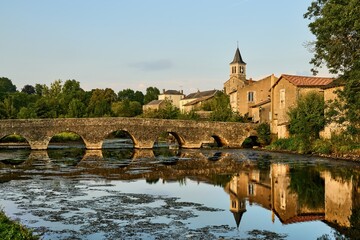 the church of Sanxay and the medieval arched stone bridge are reflected in the water surface of the river Vonne
