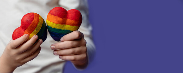Closeup of rainbow painted hearts in hands of caucasian kids on purple background. Copy space. Love togetherness and saint valentine concept