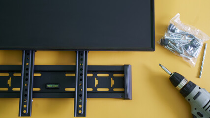 Bracket for wall mounting a computer monitor or TV, screwdriver, mounts and monitor screen on yellow background. Concept of wall mounting a computer monitor or TV in the interior