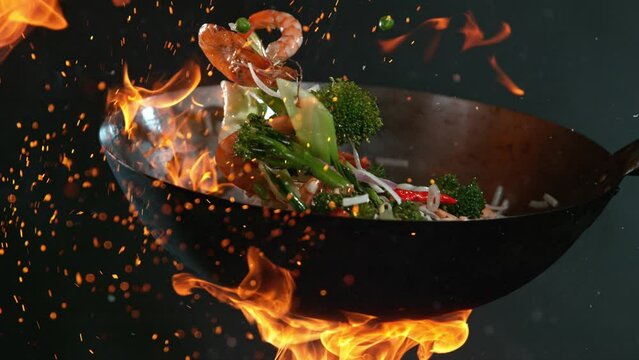 Super Slow Motion Shot of Wok Pan with Flying Ingredients in the Air and Fire Flames. Filmed on High Speed Cinema Camera at 1000 FPS.