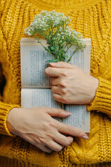 Female in sweater is holding book and bouquet. Warm knitted sweater in mustard color. Open paper...