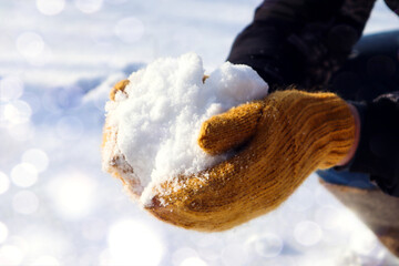 Winter games: hands in bright yellow mittens, ready to make a snowball, close-up, space for text