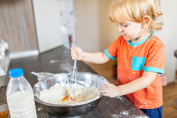 Little kid is mixturing dough with whisk at kitchen. Child boy is preparing dough - mixing...