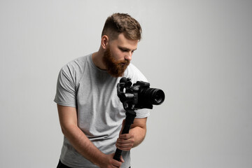 Filmmaking, hobby and creativity concept. Professional male videographer shooting video using modern dslr camera on 3-axis gimbal over white wall.