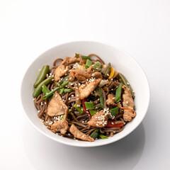 Bowl of asian food. Buckwheat brown noodles with meat fillets, onions and sesame seeds isolated on white background. Pan-Asian cuisine. Soft focus.