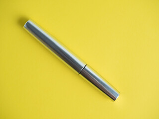 close-up of a closed mascara of silver color on a bright yellow background.