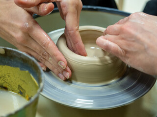 Close-up of people's hands making an object out of raw clay on a potter's wheel. Conducted master classes and workshops. Hobby, selective focus