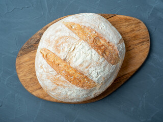 Close-up of fresh crispy wheat bread of round shape on a wooden cutting board. Grey background. Top view ,flat lay