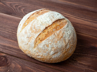 Close-up of a round loaf of wheat bread lying on a brown wooden background. Baking, bakery concept. Top view, flat lay