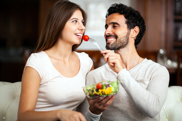 Man spoon feeding salad his girlfriend on a sofa