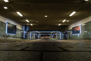 A tunnel underground for bikers and pedestrians, bikers in the back riding their bikes and having their lights on. The lights in the tunnel reflection in the walls