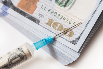 Closeup shot of a plastic syringe filled with a rolled dollar banknote lying on a stack of money.