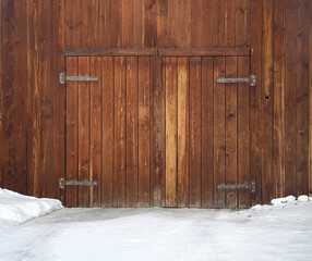 Old wooden gates, iron hinges in snow. Faded, unpainted gates, in winter.