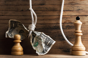 Wooden chessmen and crumpled dollar bill hanging on a tightly knotted white rope.