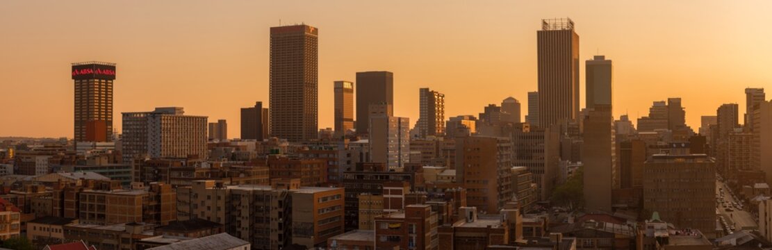 A horizontal panoramic cityscape taken during a golden sunset, of the central business district of the city of Johannesburg, South Africa