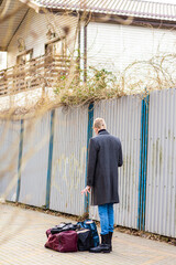 Fototapeta premium young male tourist in a coat with a suitcase of arrival or departure in the park looking for geolocation in the phone