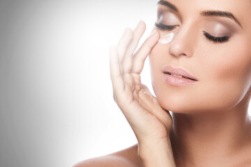 Obraz na płótnie Canvas Beautiful woman applying moisturizing cream under her eye