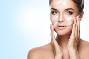 Beautiful woman applying moisturizing cream on her face