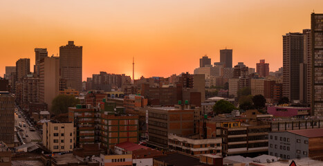 Fototapeta premium A horizontal panoramic cityscape taken at sunset, against an orange sky, of the central business district of the city of Johannesburg, South Africa