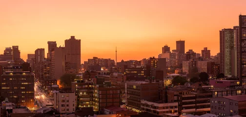  A horizontal panoramic cityscape taken after sunset, against a pink and orange sky, of the central business district of the city of Johannesburg, South Africa © Udo Kieslich