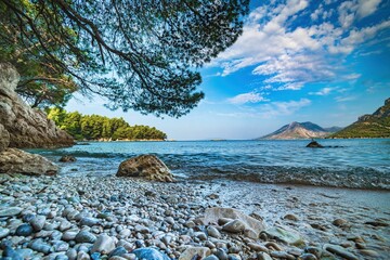 Wybrzeże i morze Chorwacji z kamienną plażą i niebieskim niebem z białymi chmurami - obrazy, fototapety, plakaty