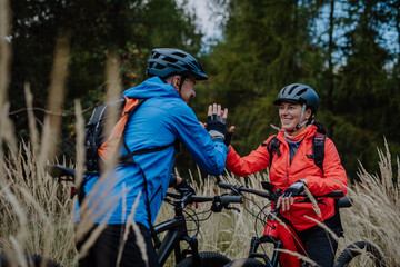 Senior couple bikers high fiving outdoors in forest in autumn day.