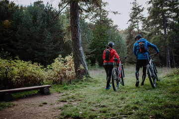 Fototapeta premium Rear view of senior couple bikers walking and pushing e-bikes outdoors in forest in autumn day.