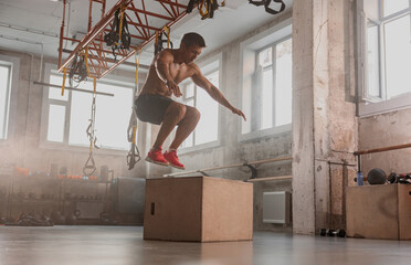 Side view of male athlete jumping on wooden box during sport training in fitness center