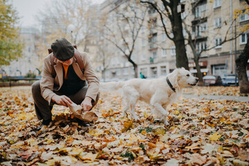 Senior man cleaning his dog's waste outdoors in park on autumn day.