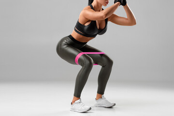 Fototapeta na wymiar Fitness woman doing exercise for glute with resistance band on gray background. Athletic girl squats