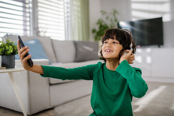 Happy multiracial boy with headphones and smartphone listening to music at home.