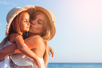A mother with a child in motion throws up a girl on the seashore in a straw hat, happy emotions