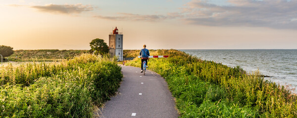 Girl cycling towards lighthouse De Ven near Edam during sunset in North-Holland in The Netherlands