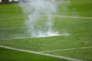 Details with the explosion of a firecracker thrown on the pitch by a supporter during a soccer game.