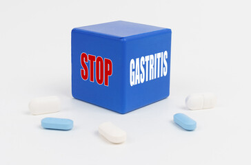 On a white surface are pills and a blue cube that says - STOP GASTRITIS