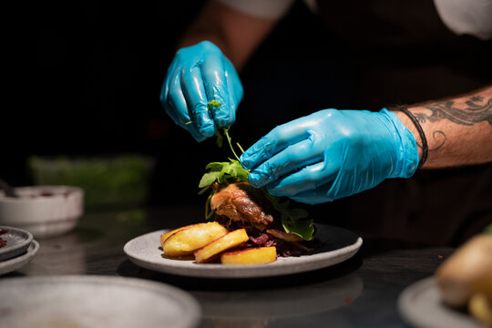 Chef's hands in gloves serving and decorating meal in restaurant kitchen