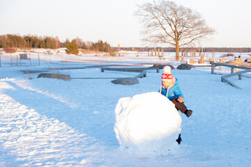 The child, a little Caucasian girl plays on the playground, makes a big snowball. Spring sun.