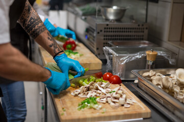Unrecognizable chef with gloves cutting vegetables indoors in restaurant kitchen.