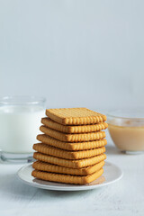 Fototapeta na wymiar cookies with cup of tea.stacks of tasty cookies with glass of milk on the white plate. square biscuits on the white table with copy space. healthy eating. vertical
