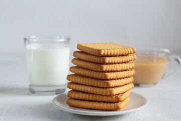 Fototapeta na wymiar glass of milk and cookies.stacks of tasty cookies with tea on the white plate. square biscuits on the white table with copy space. healthy eating.