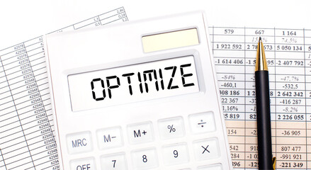 On the desktop there are reports, a white calculator with the text OPTIMIZE on the scoreboard and a pen. Business concept.
