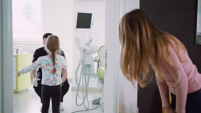 Little girl patient enters the dental office and says goodbye to the doctor