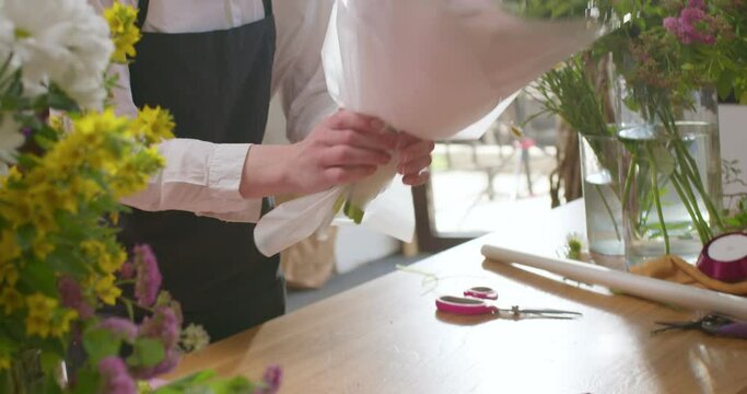 Cropped florist female finishing flower arrangement. Fresh cut flowers for customers, clients. European floral shop. Delivery fresh cut flower. Talented woman in black apron working in flower shop