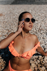 A beautiful young woman in glasses and a bikini is sitting on the ocean and enjoying a vacation on a sunny day. Tourism and tourist trips. Opening borders, and vacation.